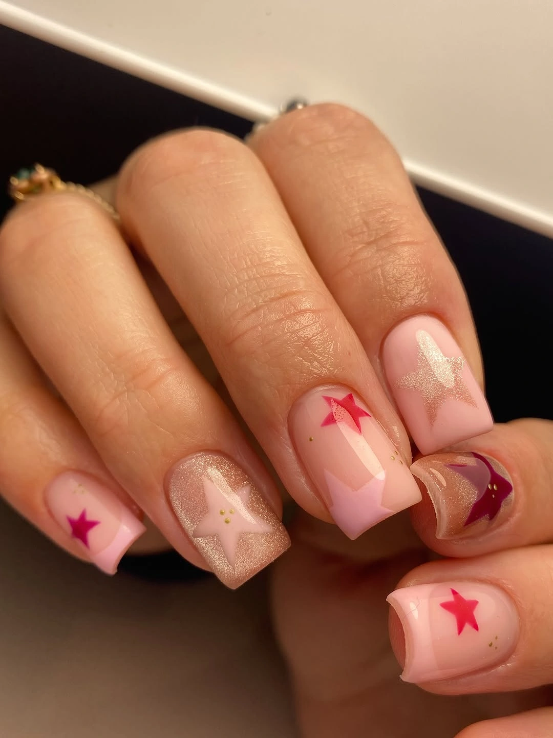 Pink square nails with red stars, champagne shimmer and pale geometric accents.