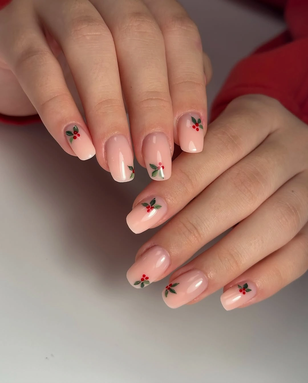 Short square pink nails with small green holly leaves and red berries.