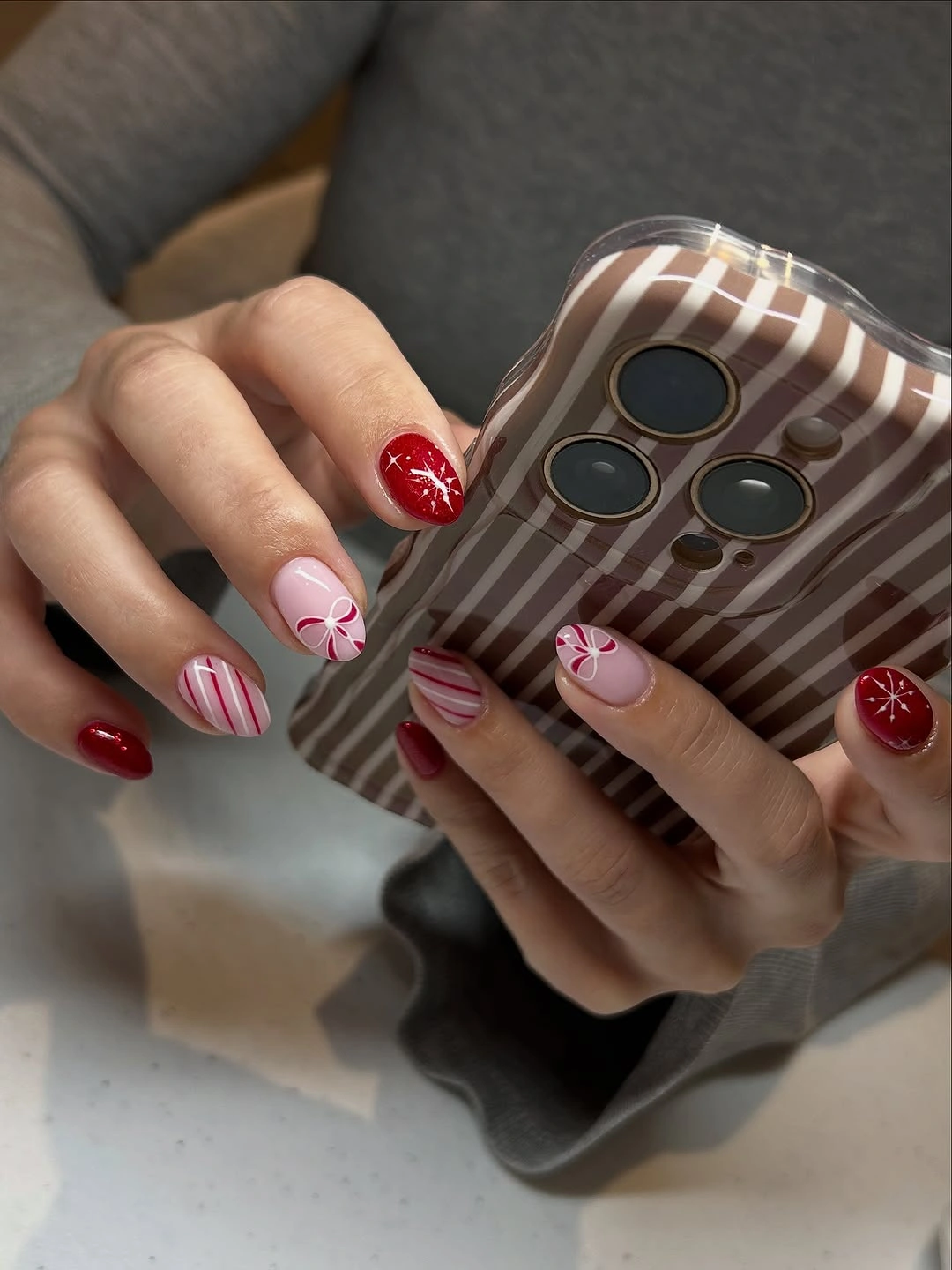 Short red and pink nails with candy stripes, ribbon motifs and white starbursts.