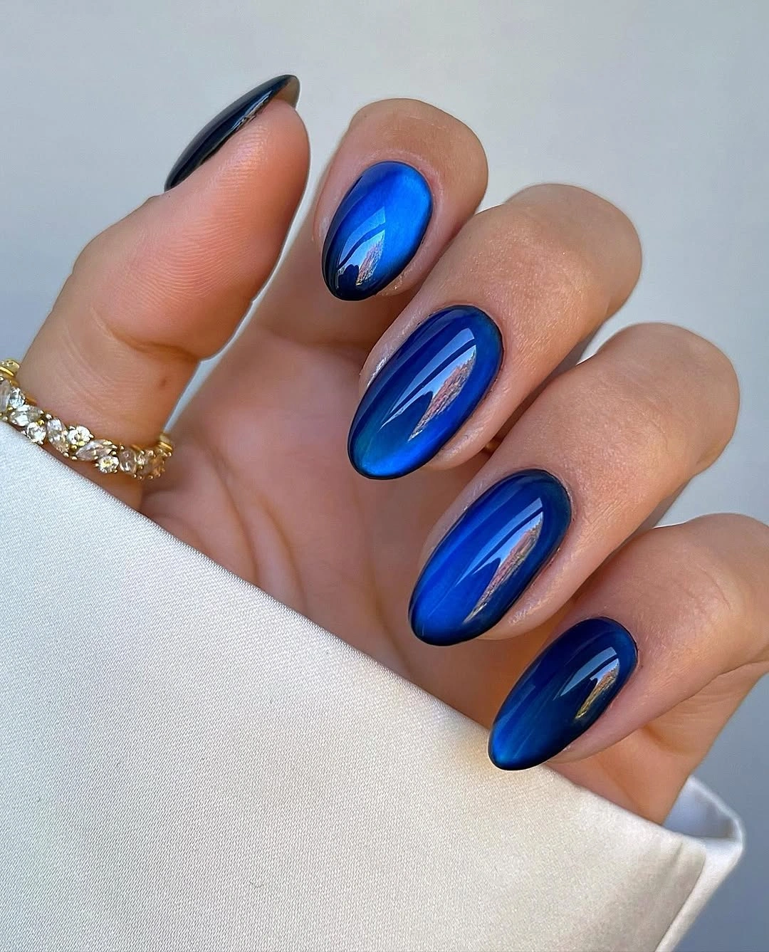 Long almond nails with reflective electric blue surfaces and dark navy edges.