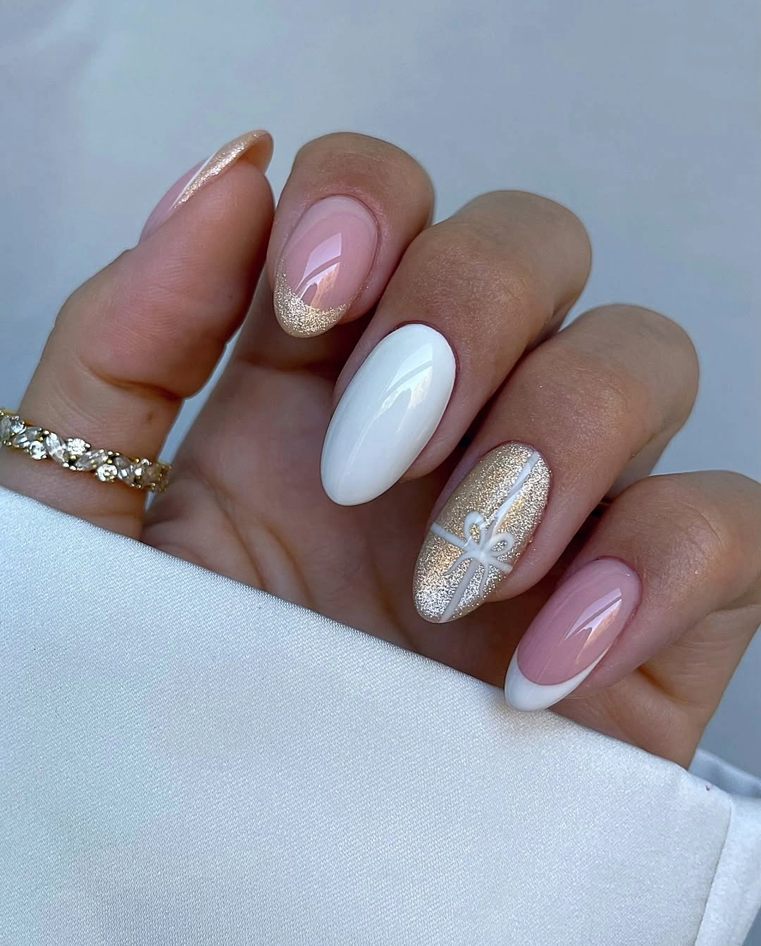 White and blush almond nails with gold glitter and a raised-looking white bow.