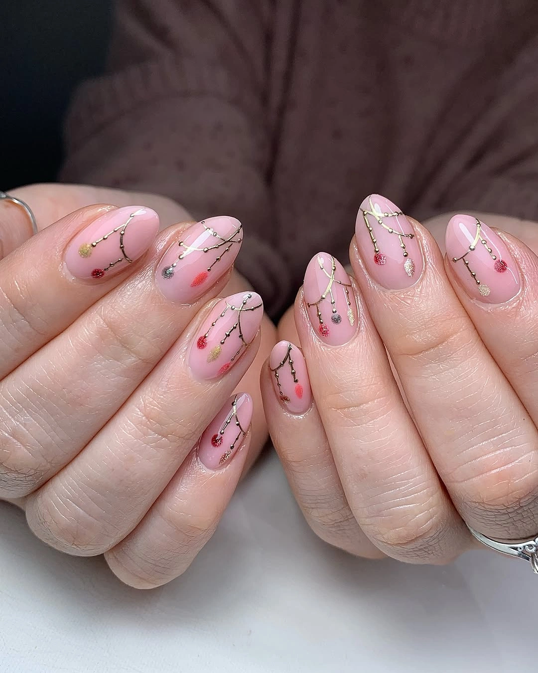Blush pink almond nails with fine garland lines and tiny colorful ornaments.