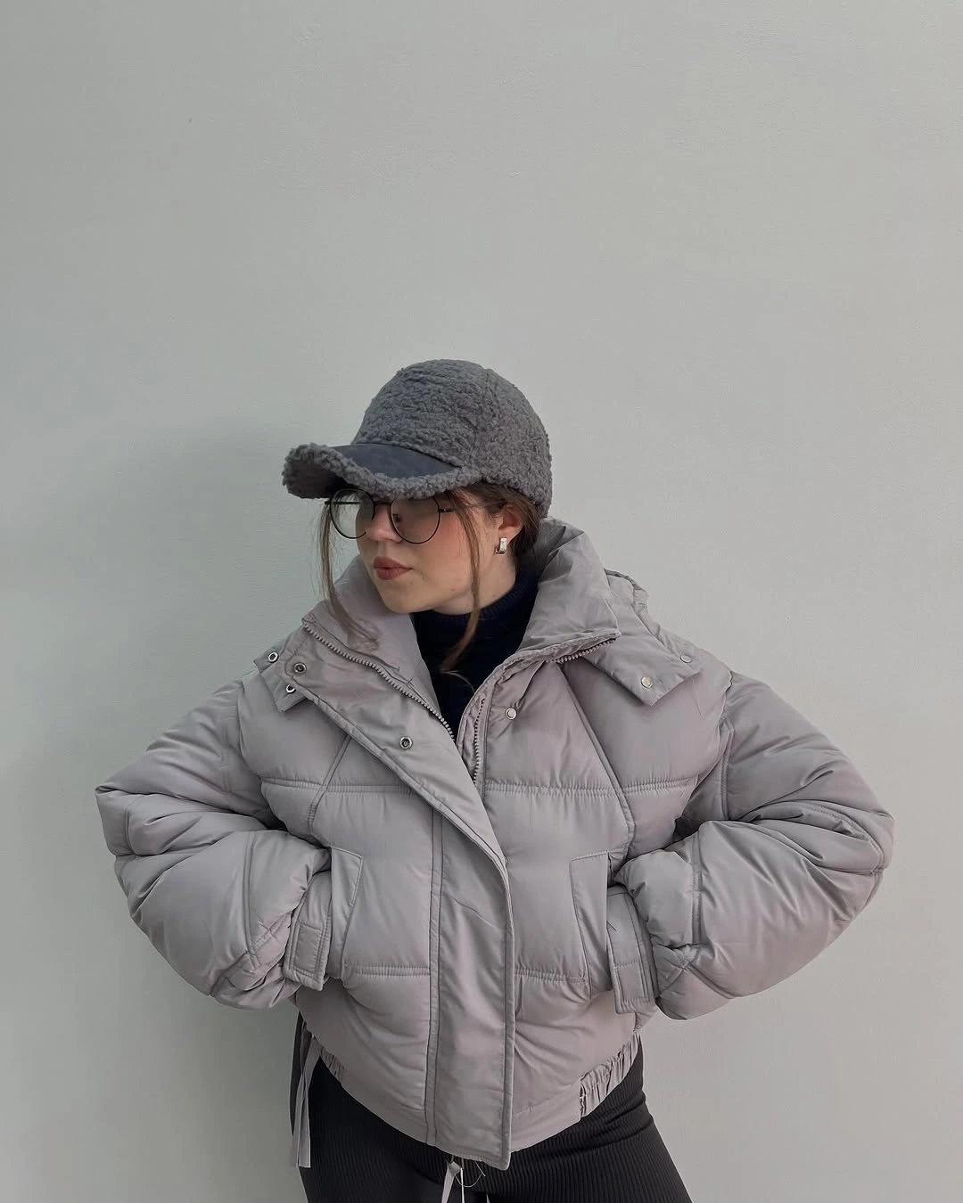 Cropped light gray puffer jacket with charcoal textured cap and glasses.