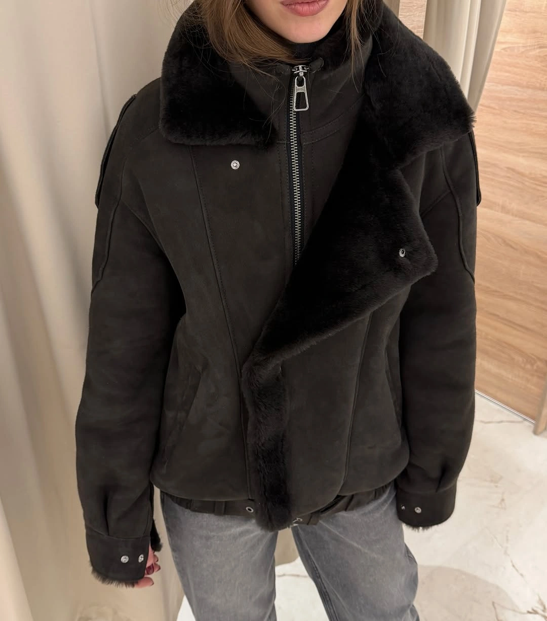 Dark shearling-look jacket with black plush collar and faded gray jeans.