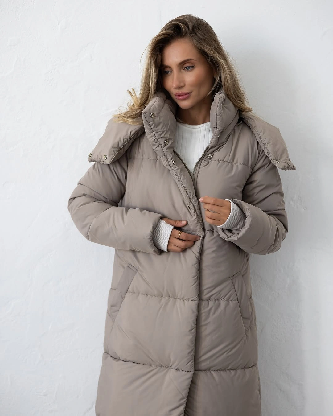 Long taupe beige quilted puffer coat over white ribbed knit sweater.