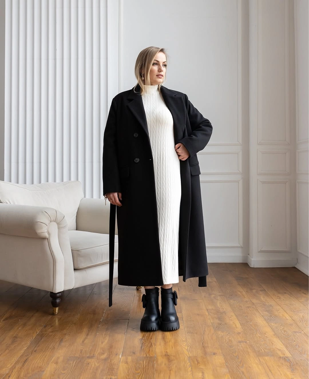 Long black coat over ivory ribbed knit dress with chunky black ankle boots.