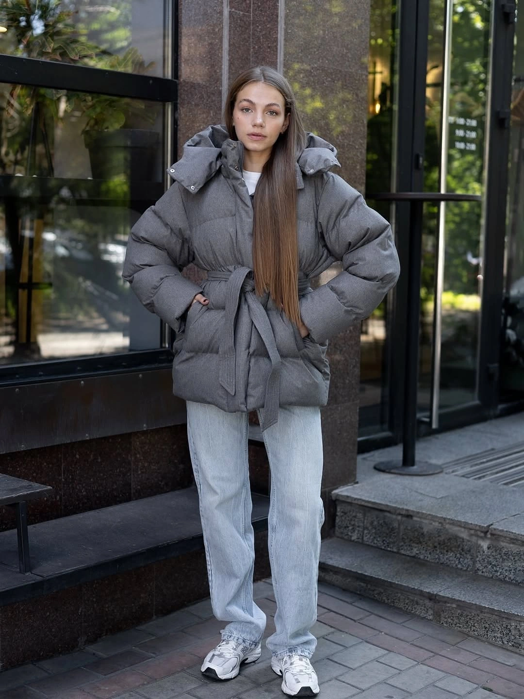Gray belted hooded puffer jacket with loose light wash jeans and sneakers.