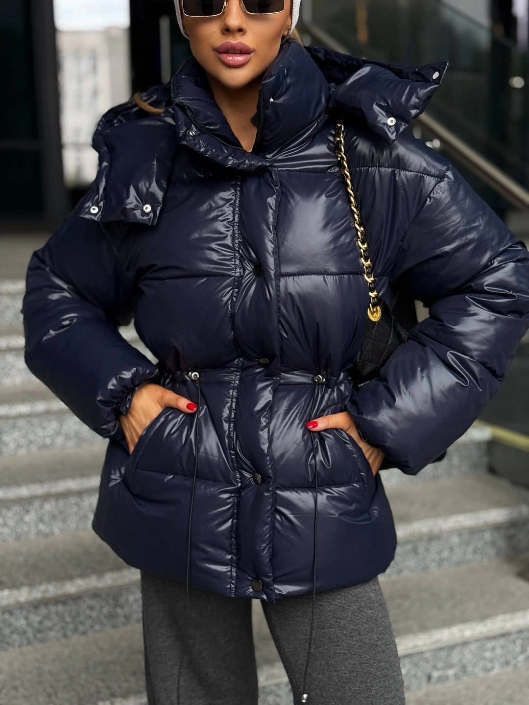 Glossy navy blue puffer jacket with gathered waist and gray trousers.